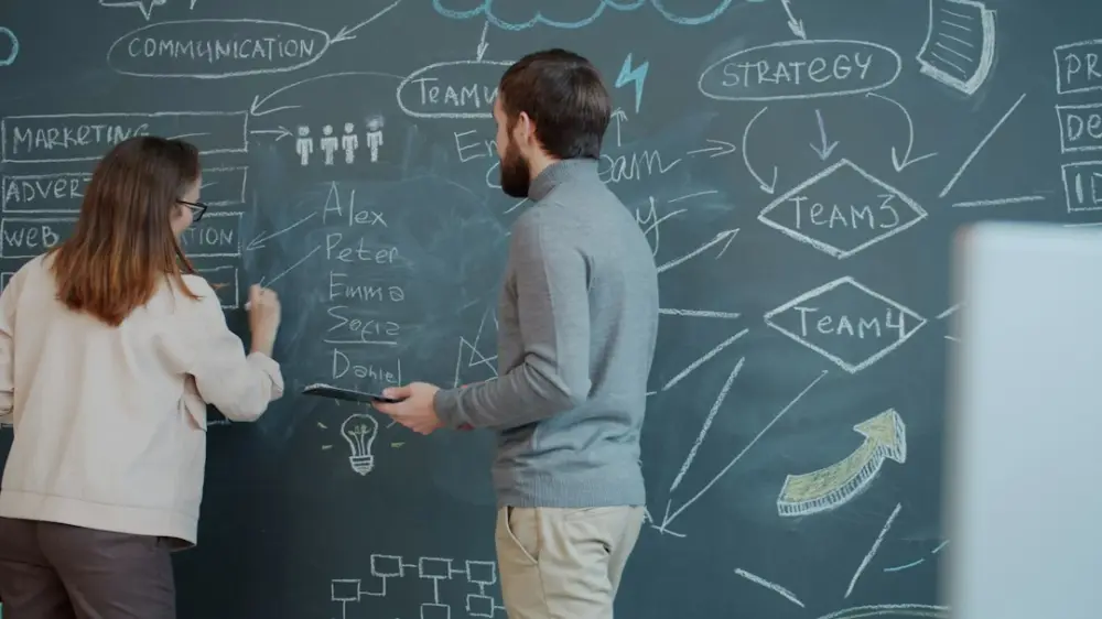 Two people planning on a chalkboard with diagrams, illustrating connecting creative choices with a clear purpose